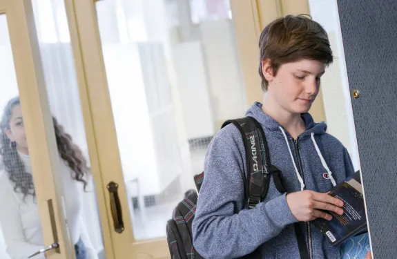 A student reads at their locker as another student enters through a school door.