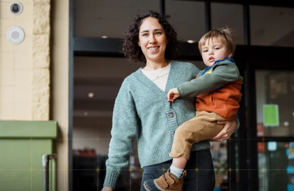 A woman stands outside of a retail store holding her son with an Axis camera in the background