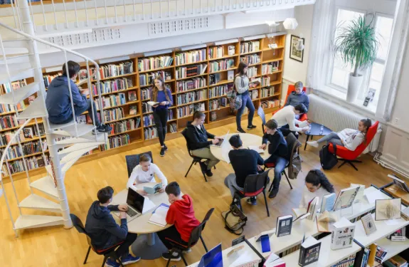 Students hang around a school library, studying and reading books.