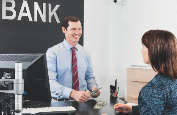 A bank teller hands cash to a customer.