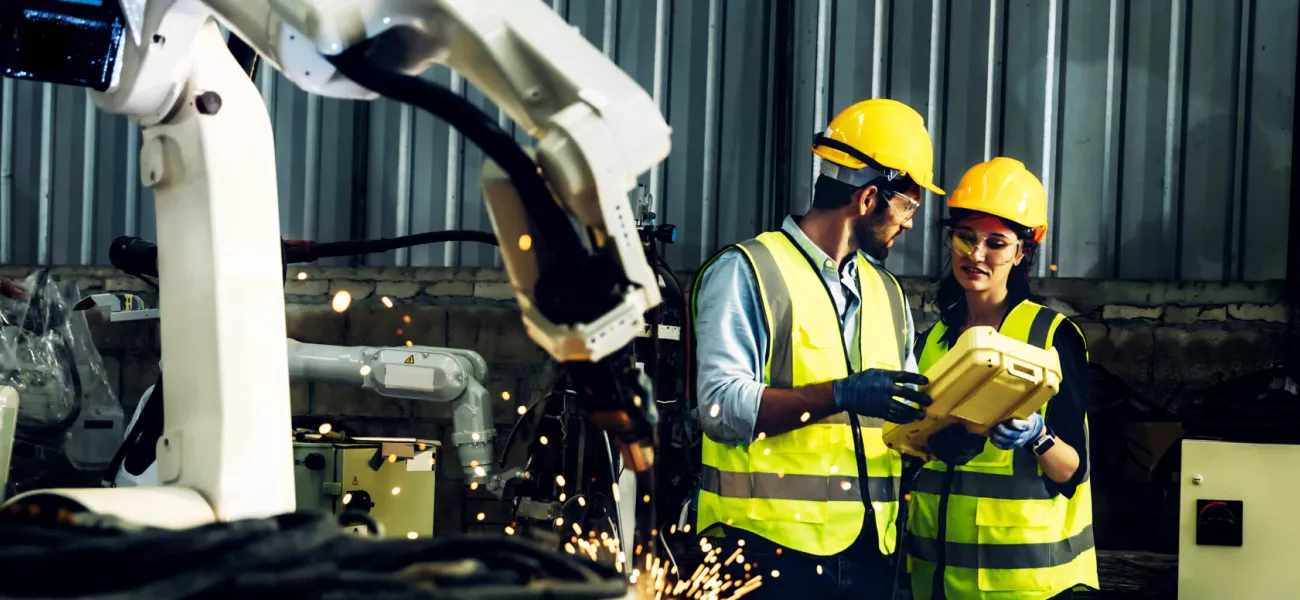 People discussing in industrial setting with robotic arm