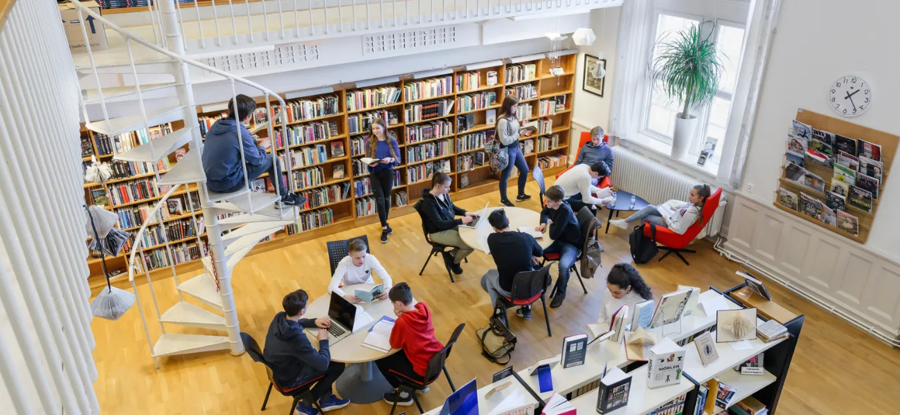 Students hang around a school library, studying and reading books.