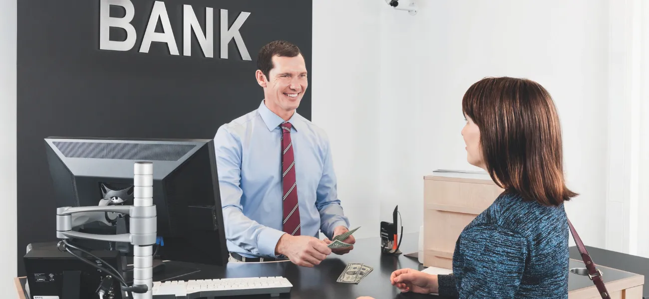A bank teller hands cash to a customer.