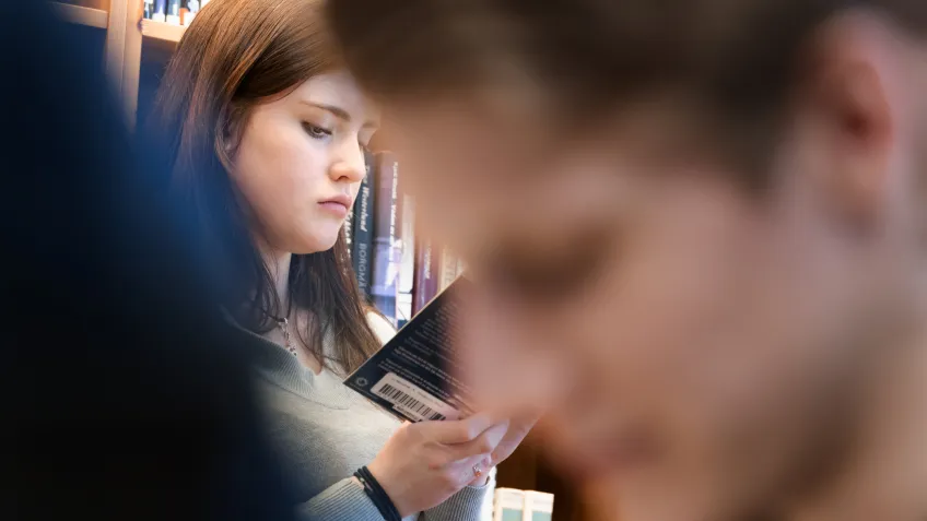 Girl in a school library, partly covered by a boy
