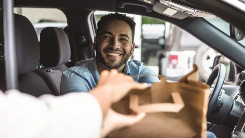 Man in a car receiving a bag of food through the car window