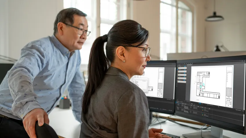 A woman and man collaborating on computer screens