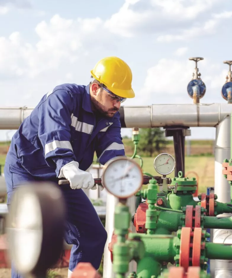 Man in hardhat adjusting oil pipes